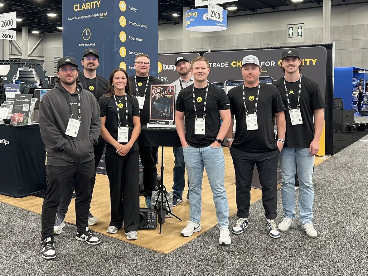 A group of eight people smiling, wearing lanyards, stands in an exhibition booth
