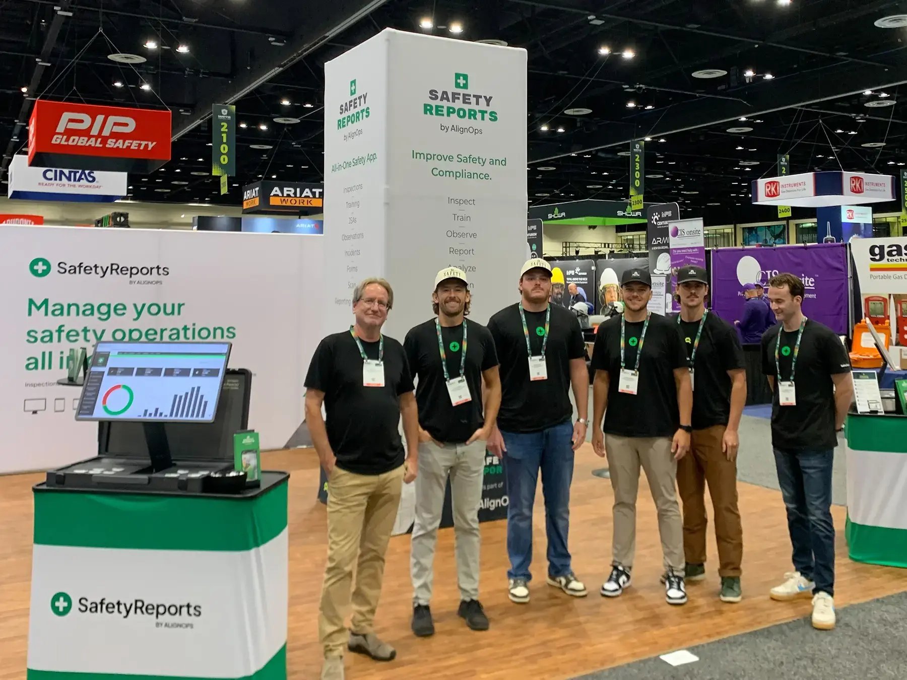 A group of six men in matching black shirts stands smiling in front of a trade show booth
