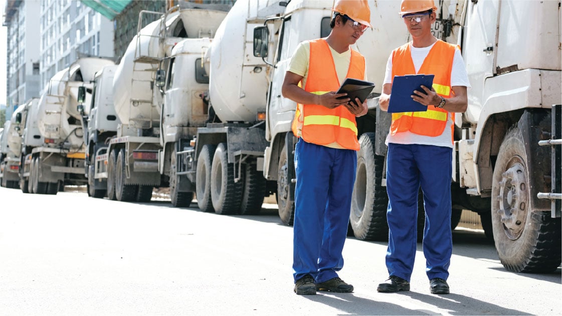 Construction workers standing next to cement trucks while holding tablets