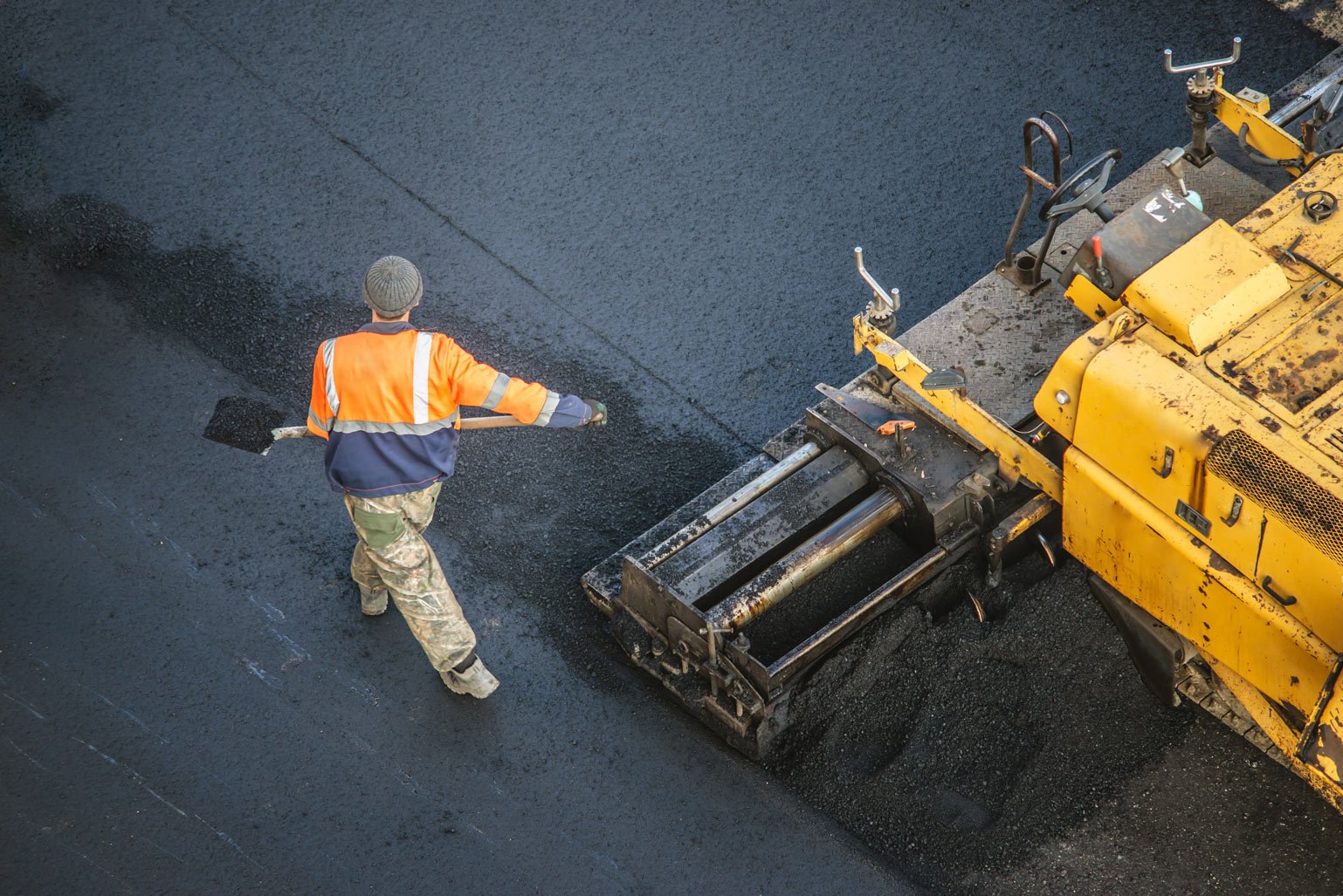 construction worker laying down asphalt with large machinery