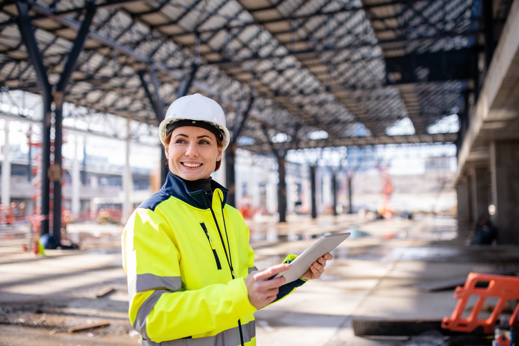 safety professional wearing a hard hat and reflective jacket while holding a tablet at a job site