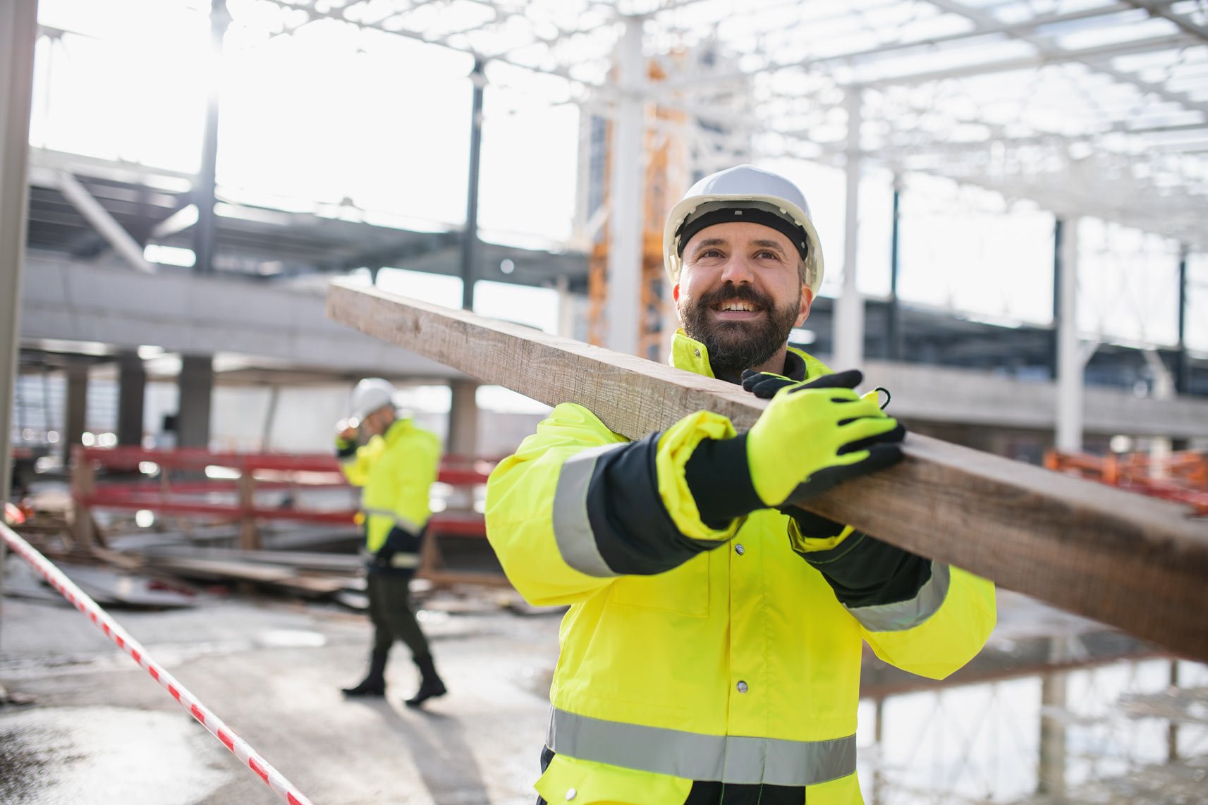 construction worker carrying a large wood beam across his shoulder
