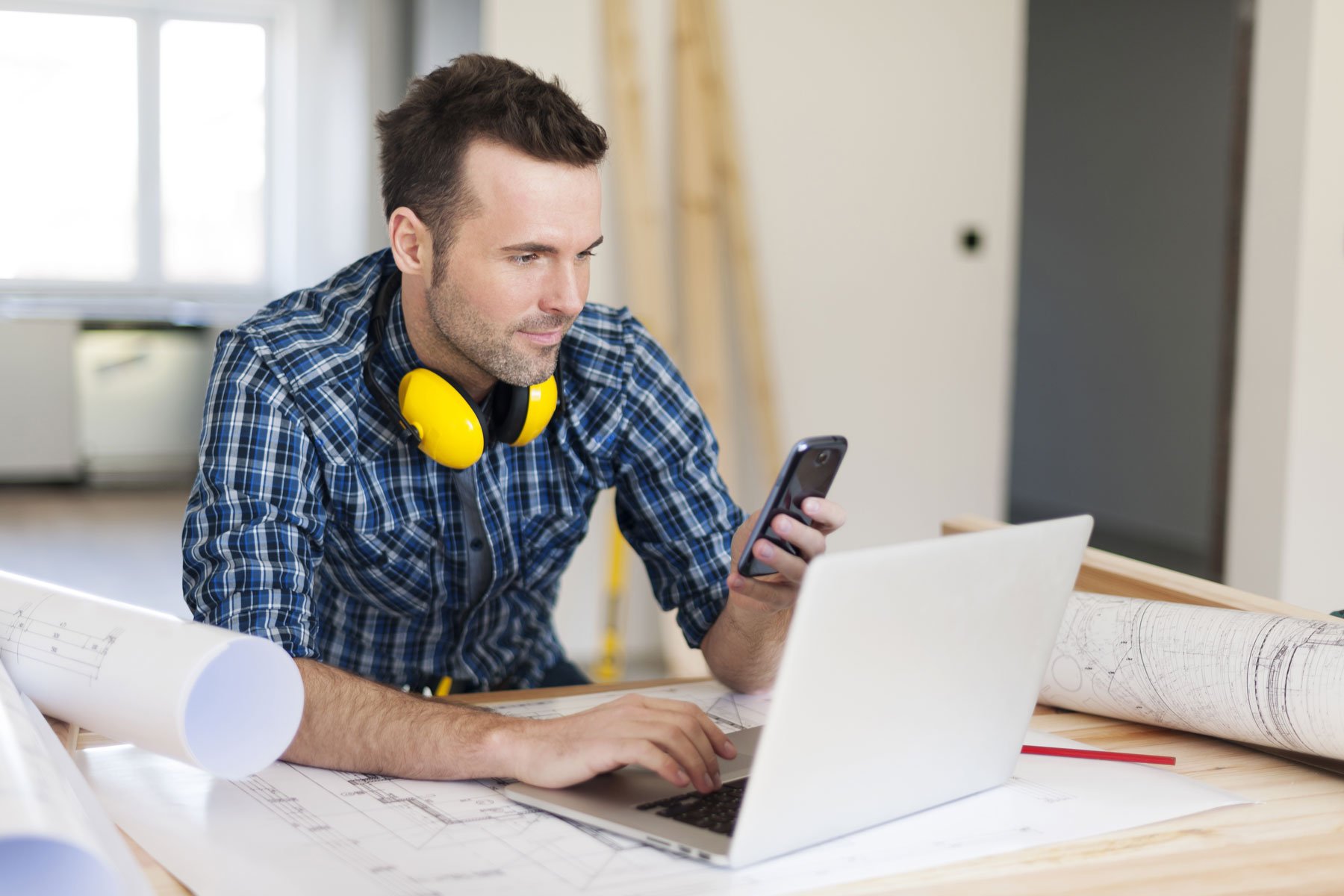 Contractor looking at cell phone while typing on a computer