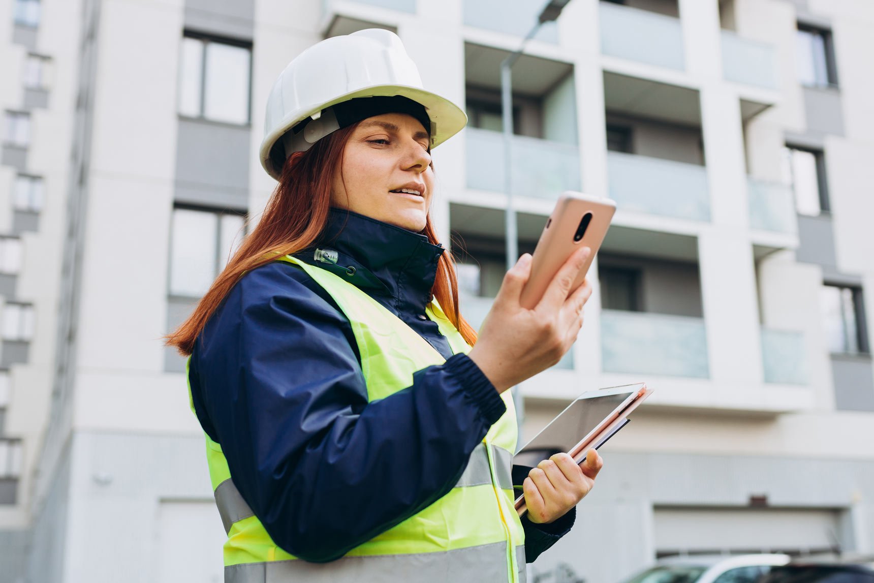 engineer at job site holding a tablet and looking at mobile phone