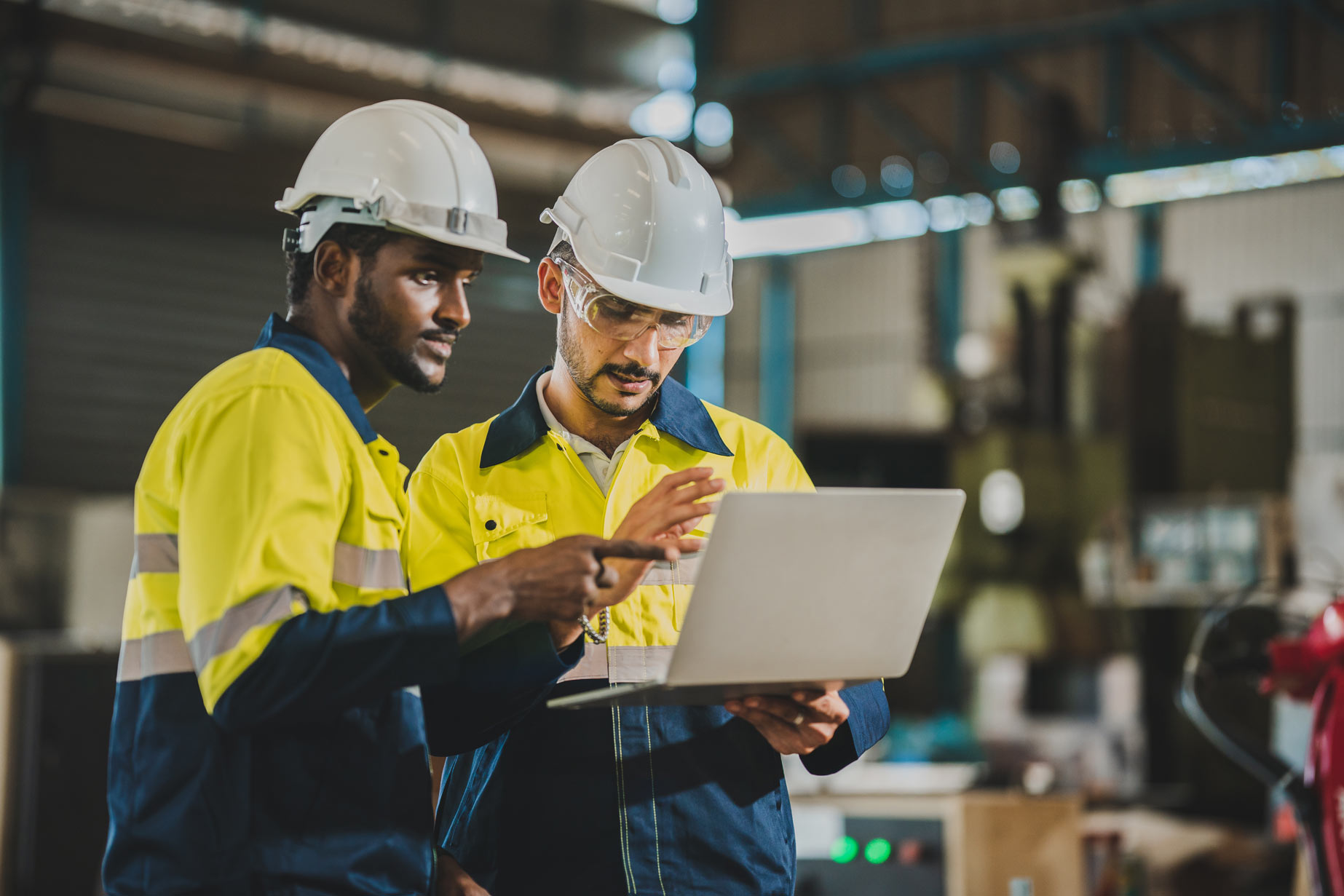 two men wearing hard hats looking at laptop