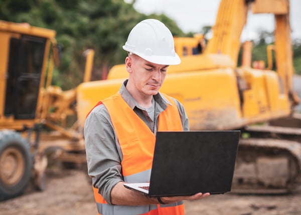construction worker on site with heavy machinery looking at laptop device