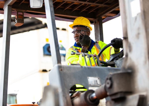construction worker wearing hard hat while talking on walkie talkie and riding a lift